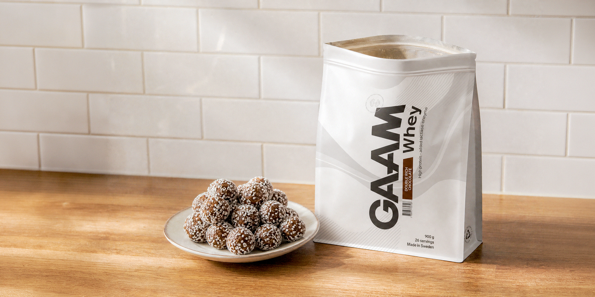 Proteinbollar med chokladsmak på ett fat bredvid GAAM Whey Double Rich Chocolate – ett enkelt recept på chokladbollar med proteinpulver.